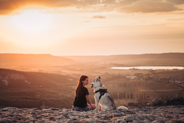 Belle fille joue avec un chien husky gris et blanc dans les montagnes au coucher du soleil