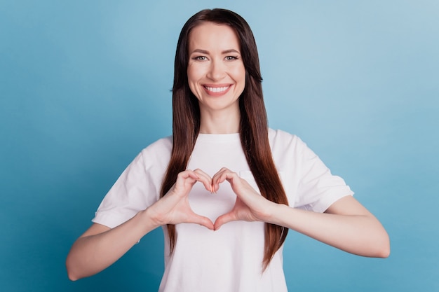 Belle fille joyeuse faire coeur avec les doigts isolés sur fond bleu