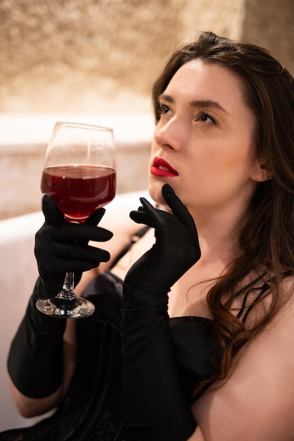 Belle fille en lingerie érotique assise dans la salle de bain avec un verre de vin