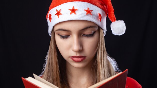 Belle fille lisant un livre sur le fond noir en tenue de nouvel an. Fête.