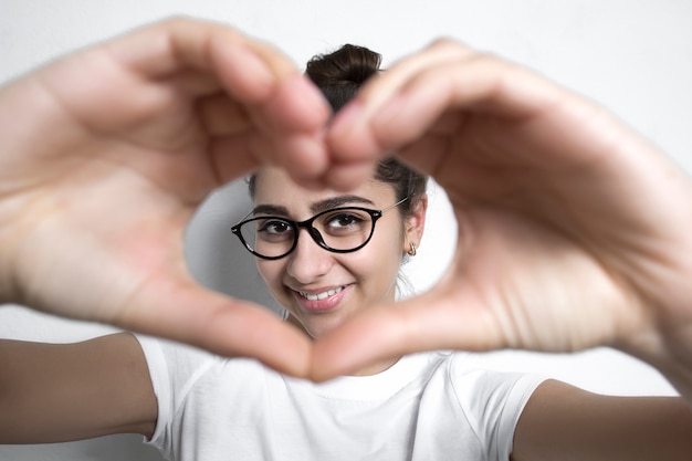 Une belle fille à lunettes fait un coeur de ses mains