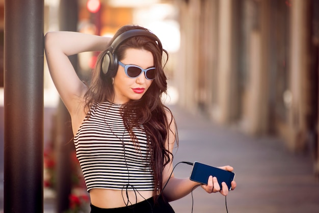 Photo belle fille avec des lunettes de soleil et des écouteurs dans la rue