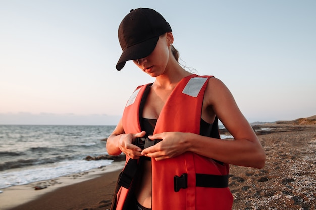 Belle fille en maillot de bain noir porte un gilet de sauvetage sur la plage