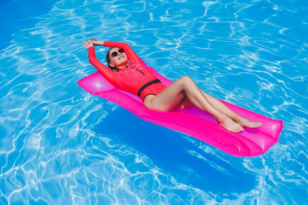 Belle fille en maillot de bain rose se reposant sur un matelas rose gonflable dans la piscine Une femme chaude et mince en lunettes de soleil et maillots de bain prend un bain de soleil Une femme se détend dans un complexe de luxe