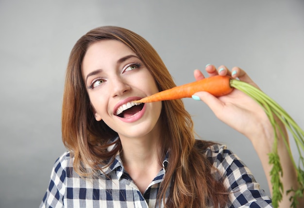 Belle fille mangeant des carottes sur fond gris