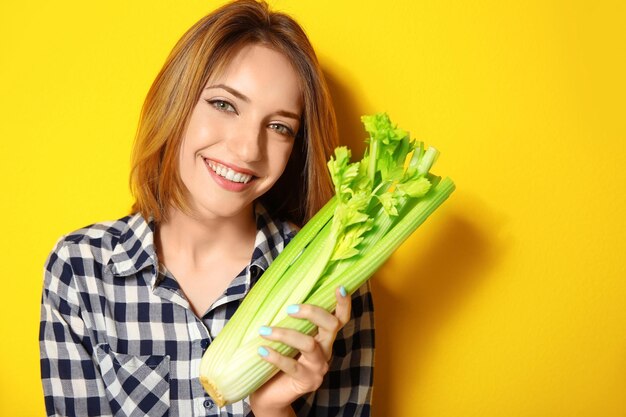 Belle fille mangeant du céleri sur fond jaune