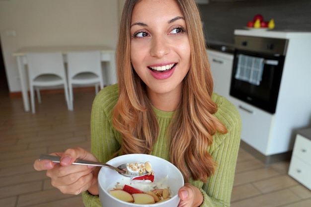 Belle fille mangeant des flocons d'avoine muesli granola avec des fruits secs et du yaourt regardant sur le côté à la maison