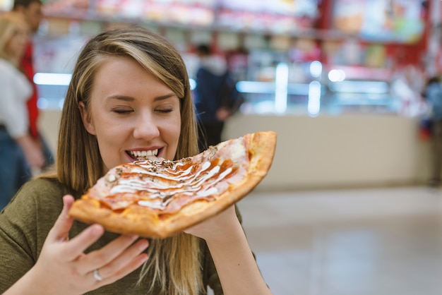 Belle fille, manger une pizza savoureuse sur fond clair. Femme heureuse, manger une pizza savoureuse.