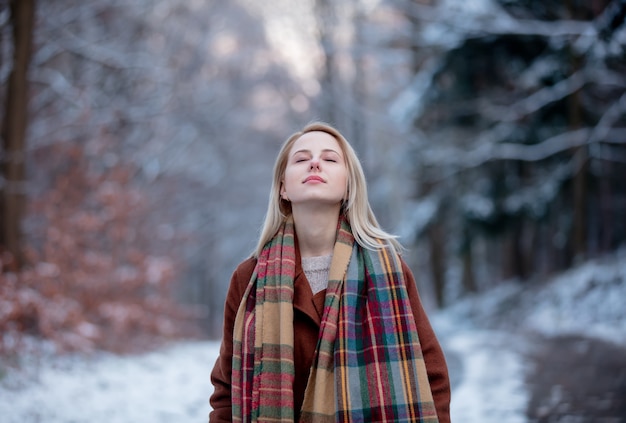 Belle fille en manteau et écharpe dans une forêt de neige