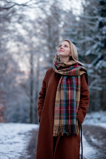 Belle fille en manteau et écharpe dans une forêt de neige