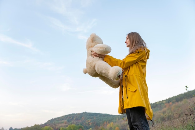 Belle fille en manteau jaune tient un ours en peluche marchant dans la nature d'automne