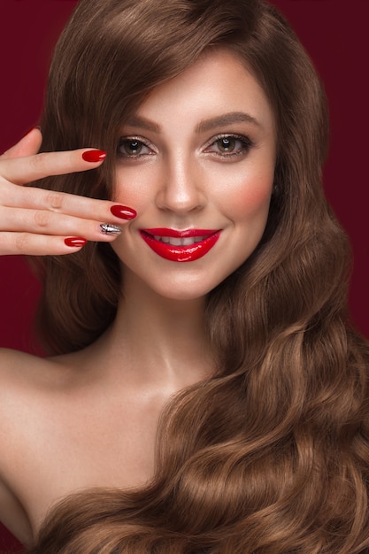 Belle fille avec un maquillage classique, des boucles de cheveux et des ongles rouges.