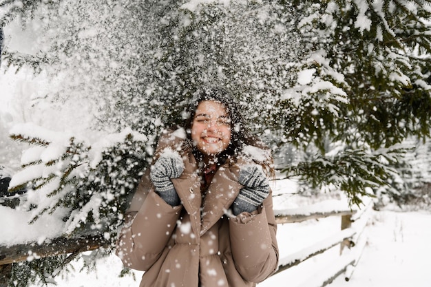 Belle fille marche dans une chute de neige. Jeune femme s'amusant dans la forêt d'hiver. Portrait en plein air de jolie femme brune posant en bois