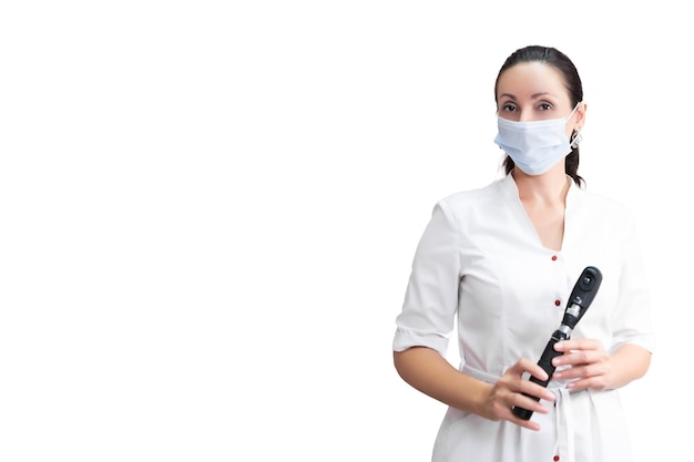 Belle fille médecin optométriste en blouse blanche et masque avec un rétinoscope à la main Isolé sur fond blanc Réception dans un magasin de lunettes de clinique ophtalmologique moderne