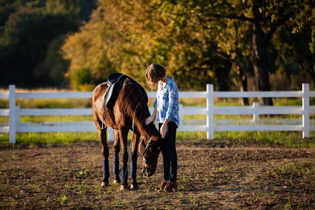 Belle fille menant son cheval brun à la ferme