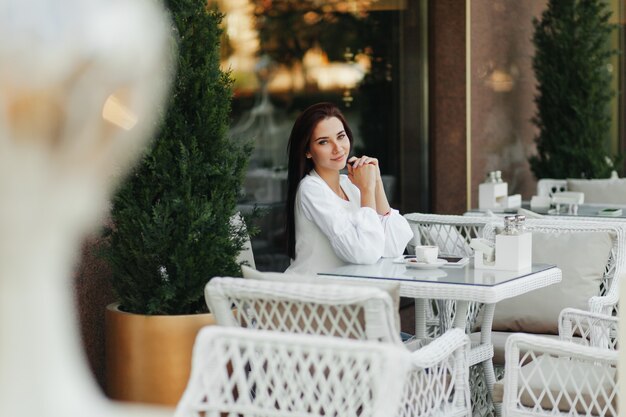 Une belle fille mignonne dans un café boit du café à une table.