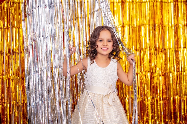 Belle fille mignonne et gaie d'enfant sur un fond de vacances d'or dans une belle robe