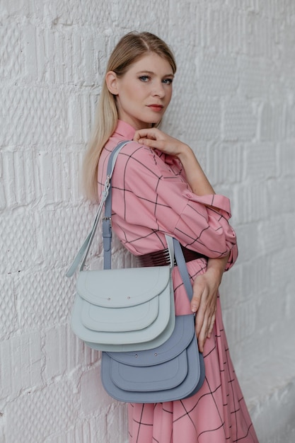 Photo une belle fille mince dans une robe rose pose contre un mur blanc elle tient deux sacs à main dans elle