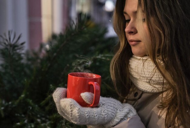Belle fille en mitaines d'hiver tenant une tasse de thé chaud à l'extérieur en hiver