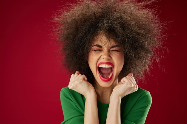 Photo belle fille à la mode avec la grimace de cheveux bouclés posant le fond rouge d'émotion inchangé