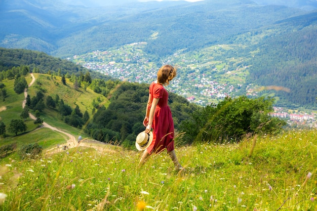 Belle fille les montagnes. Femme en robe de lin et chapeau de paille voyageant. Nature estivale incroyable autour. Concept d'harmonie et d'envie de voyager. Style naturel rustique. Vent soufflant pour photo dynamique.