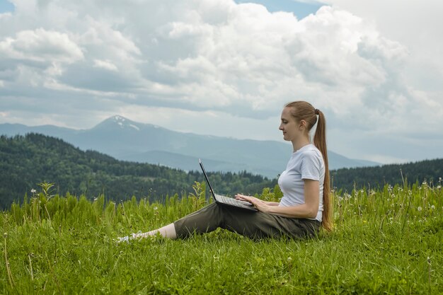 Belle fille avec un ordinateur portable assis sur l'herbe verte