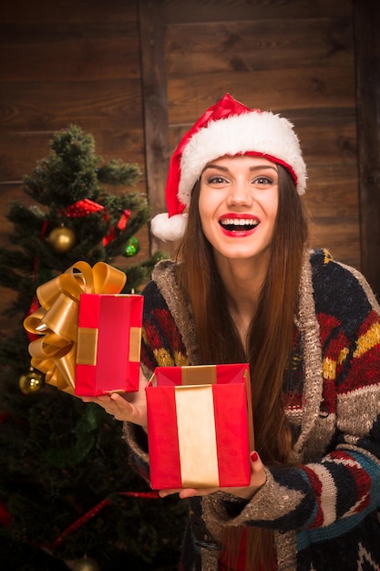 Belle fille ouvrant un cadeau et riant avec excitation près de l'arbre du Nouvel An. Heureuse dame aux lèvres rouges célébrant Noël.