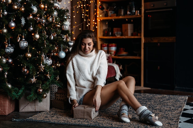 Belle fille ouvre une boîte avec un cadeau de Noël, assis sous l'arbre