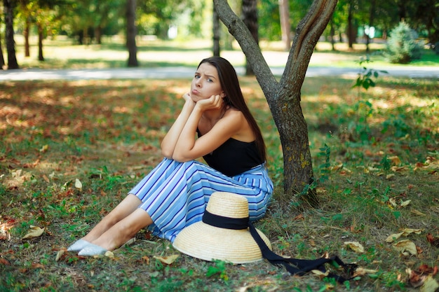 Une belle fille par temps d'été ensoleillé est assis sous un arbre avec un regard offensé.