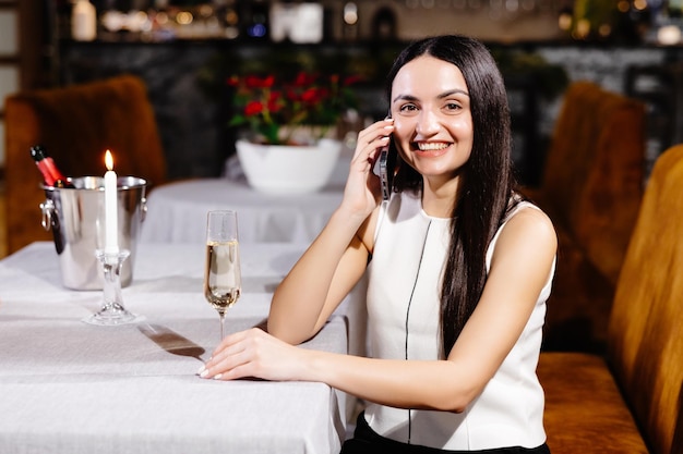 Belle fille parlant au téléphone dans un restaurant et buvant du champagne