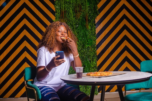 Belle fille parlant dans un café au téléphone mange de la pizza