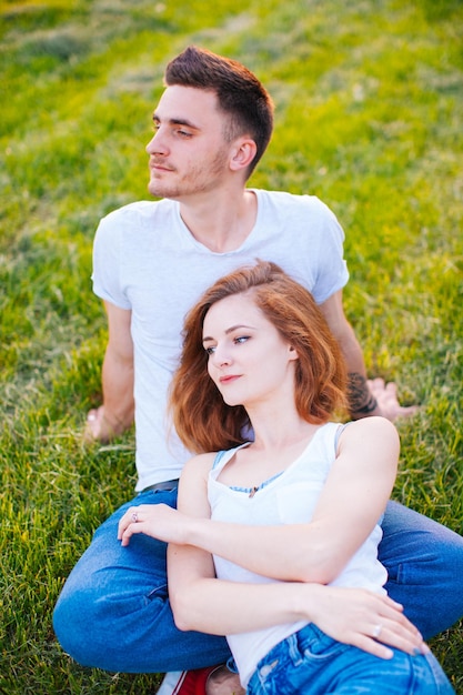 La belle fille avec le petit ami se reposant dans le parc s'asseyant sur l'herbe et rêvant