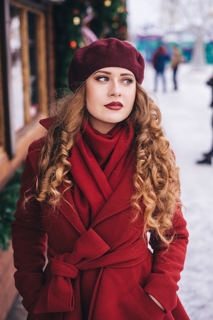 Belle fille portant un manteau rouge et un béret dans la rue de Noël