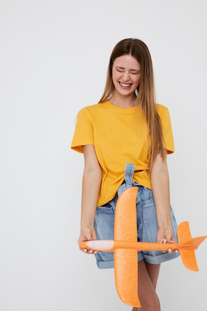 Belle fille posant un avion jaune dans les mains de fond isolé amusant