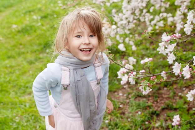 Belle fille préadolescente aux longs cheveux blonds profiter de la floraison des pommes de printemps. Petite fille d'âge préscolaire dans les fleurs des arbres de jardin. Printemps. Copier l'espace