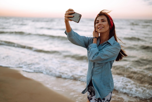 Belle fille prend un selfie sur la plage au coucher du soleil Le concept de voyage relaxant et de vacances d'été
