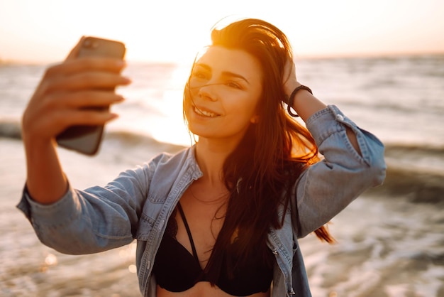 Belle fille prend un selfie sur la plage au coucher du soleil Le concept de voyage relaxant et de vacances d'été