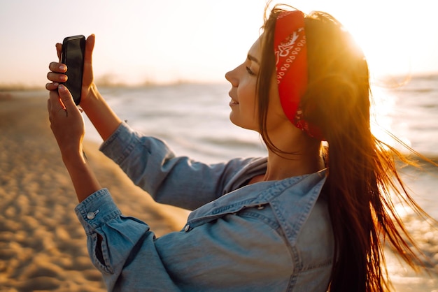 Belle fille prend un selfie sur la plage au coucher du soleil Le concept de voyage relaxant et de vacances d'été