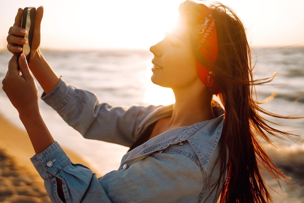 Belle fille prend un selfie sur la plage au coucher du soleil Le concept de voyage relaxant et de vacances d'été