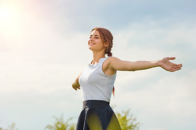 Belle fille, profitant du soleil avec ses bras tendus dans le champ contre le ciel