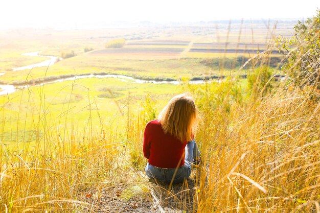 Belle fille profitant de la vue sur la nature. Hipster sur la colline. Rivière et champ en contrebas. Saison de l'automne. Femme élégante à l'extérieur. Notion touristique. Voyage découvrir le monde.