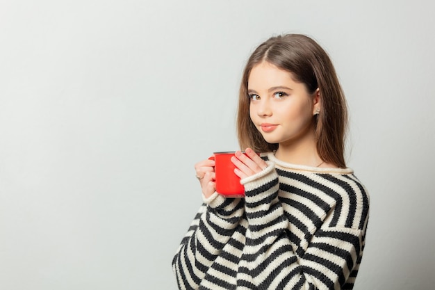 Belle fille en pull rayé avec mug rouge sur fond blanc