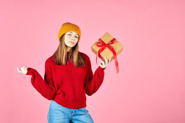 Belle fille en pull rouge confortable tenant des coffrets cadeaux dans les mains et choisissant le cadeau