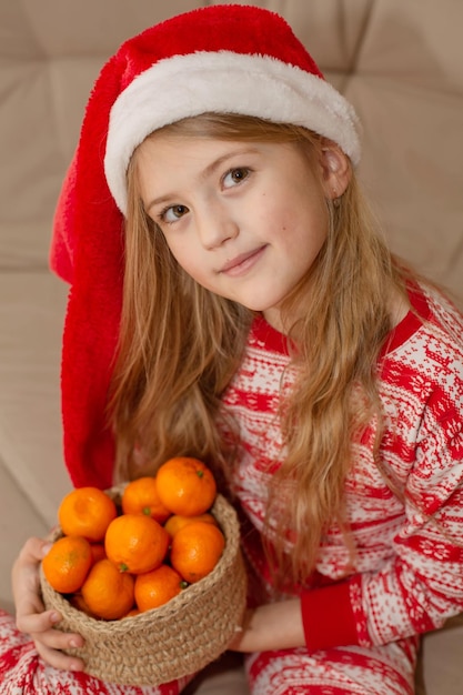 une belle fille en pyjama du Nouvel An et un bonnet de Noel tient un panier de mandarines dans ses mains