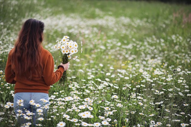 Belle fille ramasse des marguerites en journée d'été dans un champ lointain