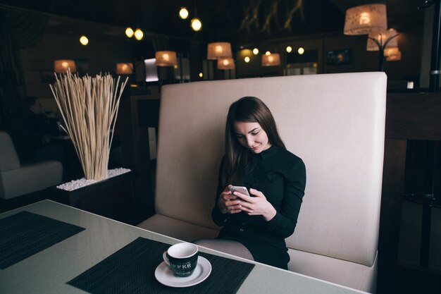 Belle fille regardant son téléphone, assis sur le canapé dans un café