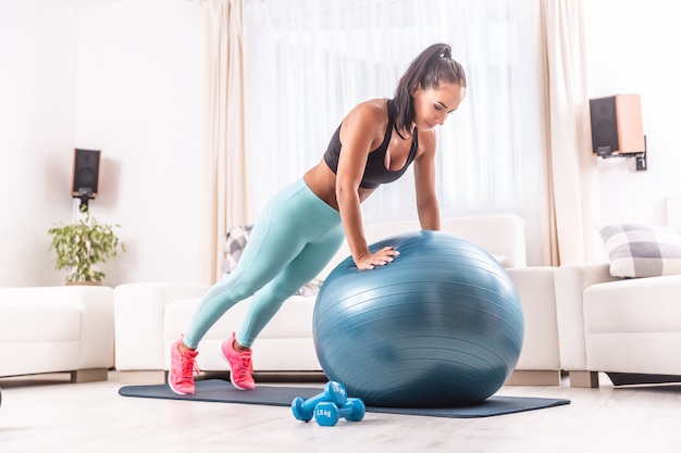 Belle fille de remise en forme fait un entraînement à domicile sur une balle en forme tenant la position de la planche