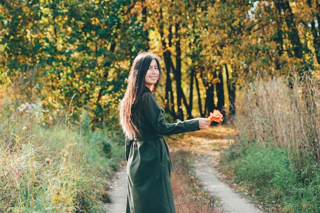 Belle fille rêveuse avec de longs cheveux noirs naturels au soleil sur fond avec des feuilles colorées.