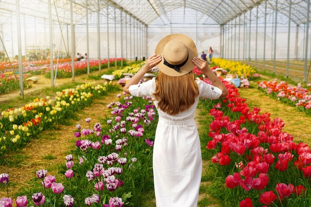 Belle fille avec une robe blanche et un chapeau de paille marchant entre des tulipes colorées au printemps