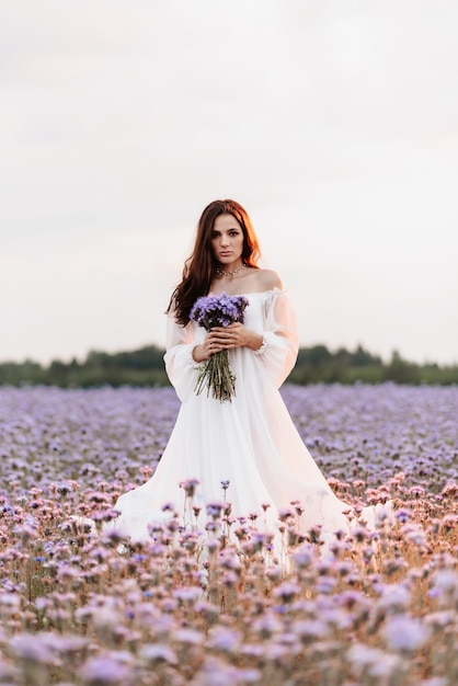 Une belle fille en robe blanche dans un champ fleuri de Provence dans une ambiance romantique avec un bouquet dans ses mains